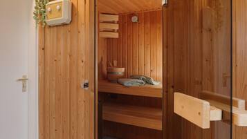 A wooden sauna with a bench, a bucket, and a towel.