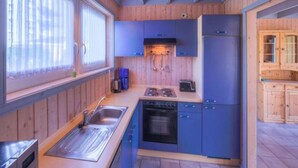 A compact kitchen with wooden walls, a sink, a stove, and cabinets. - Ferienhaus im Skandinavischen Stil (Rechlin)