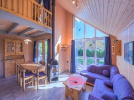 Interior de una cabaña de madera con comedor, sofá y un ventanal con vistas al exterior.