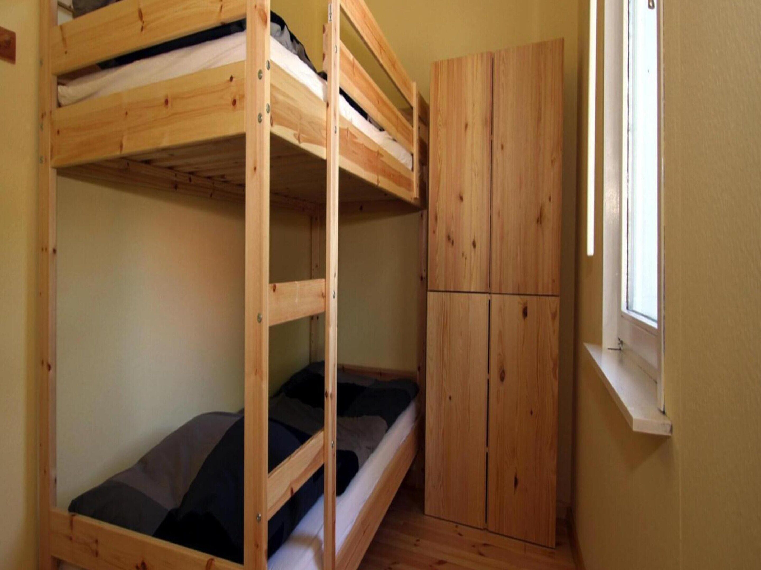 A bunk bed with a lower bunk, a wardrobe, and a window with daylight.