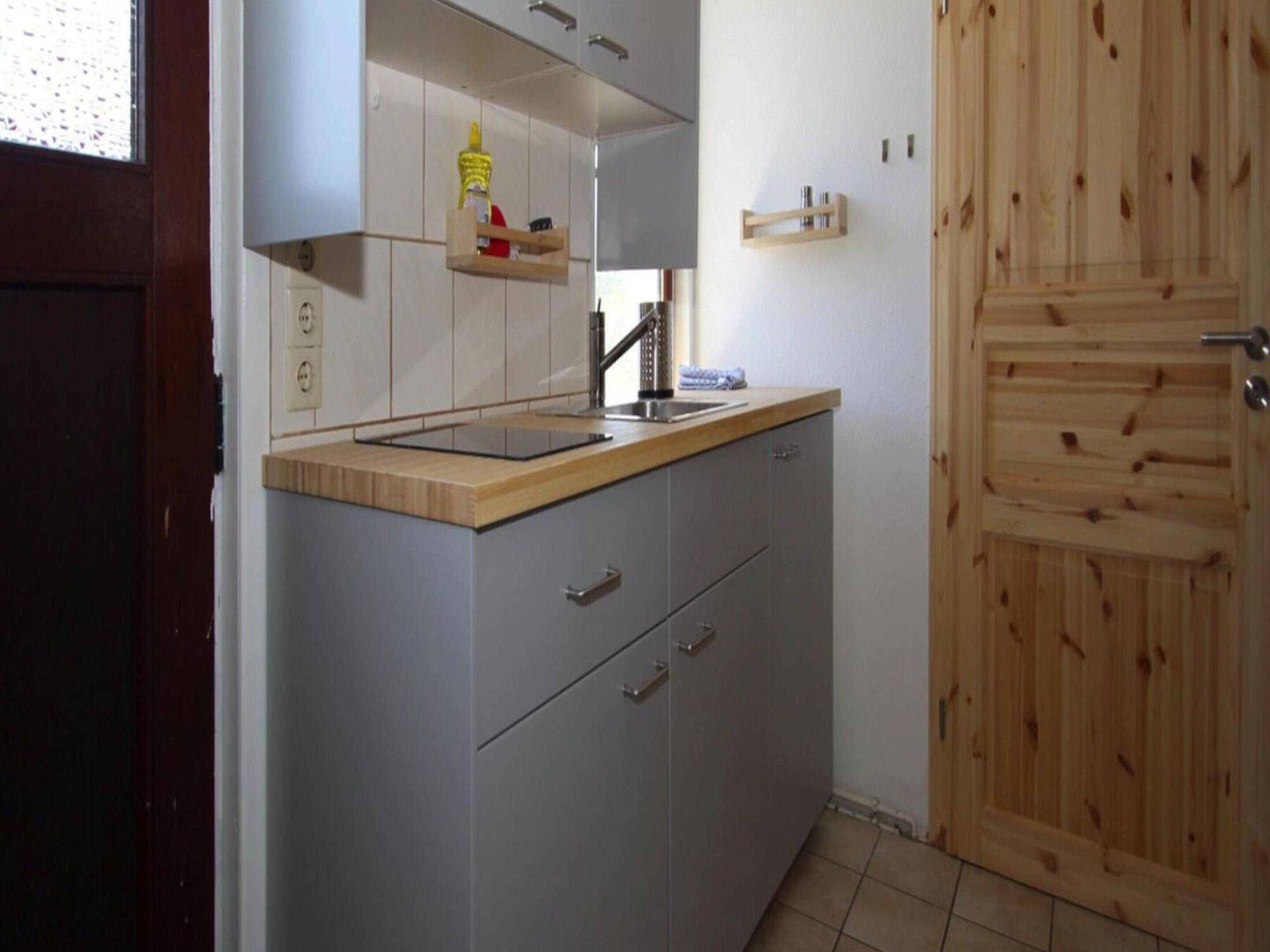 A kitchen with a wooden countertop, grey cabinets, and a wooden door.