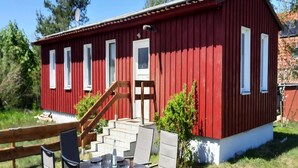 Un edificio rojo con una escalera que lleva a una puerta, una mesa con sillas al frente y una valla de madera al fondo.