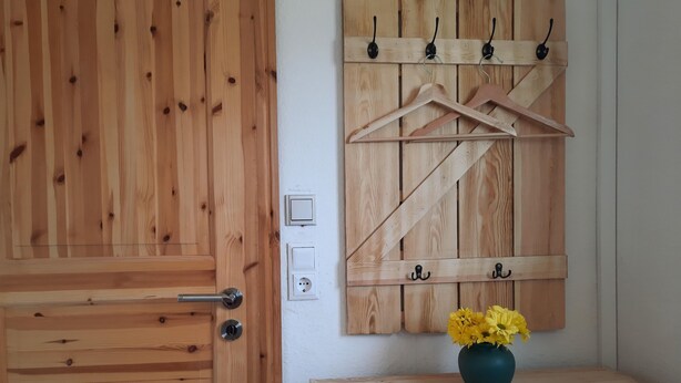 Una puerta de madera con manija y cerradura, una pared de madera con diseño de paneles, y una pequeña mesa de madera con un jarrón de flores amarillas.