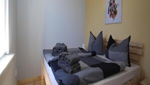 Una cama individual con estructura de madera, ropa de cama gris y una almohada.