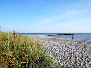 A sandy beach with a rocky breakwater in the distance, grassy dunes, and a clear blue sky. - 4 Star Holiday Home in Neuschonberg (Schönberg)