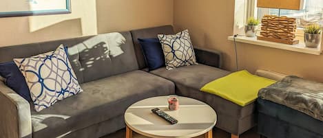 Una sala de estar moderna con un sofá gris, una mesa redonda de centro y una mesita auxiliar.