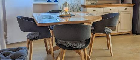 Een eetgedeelte met een houten tafel en vier stoelen, een keuken met kastjes en een aanrecht, en een raam met uitzicht.