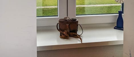 Une fenêtre donnant sur l’océan et une étagère ornée d’un pot rustique et d’un vase bleu.