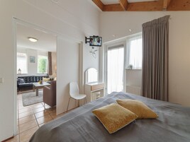 Un dormitorio con una cama, dos almohadas, un escritorio, una silla y un televisor montado en la pared.