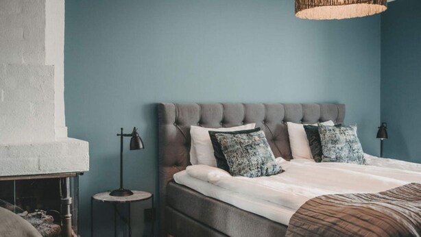 A bedroom with a tufted headboard, a bed with white bedding and patterned pillows, a bedside lamp, and a rustic fireplace. - 4 Star Holiday Home in Hisings Backa (Hisings Backa)