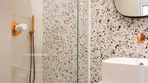A bathroom with a freestanding bathtub, a shower with a handheld showerhead, and a speckled tile wall.