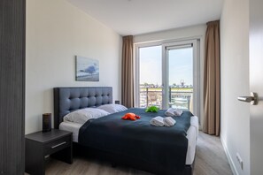 Una habitación de hotel moderna con una cama grande, una mesita de noche, una ventana con cortinas y vistas a la ciudad.