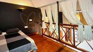 Een slaapkamer met een bed, een houten vloer, een balkon met een balustrade en uitzicht op de omgeving.