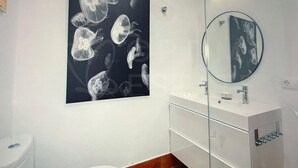Een badkamer met een witte wastafel, een ronde spiegel en een kunstwerk van kwal aan de muur.