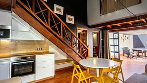 Een moderne keuken met witte kasten, een houten trap en een eethoek met gele stoelen.