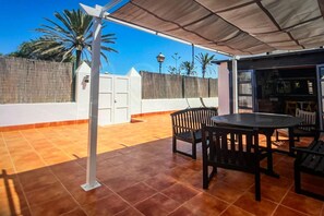 An outdoor patio with a table and chairs, a white fence, and a palm tree. - Beautiful Villa in Playa Blanca (Lanzarote)