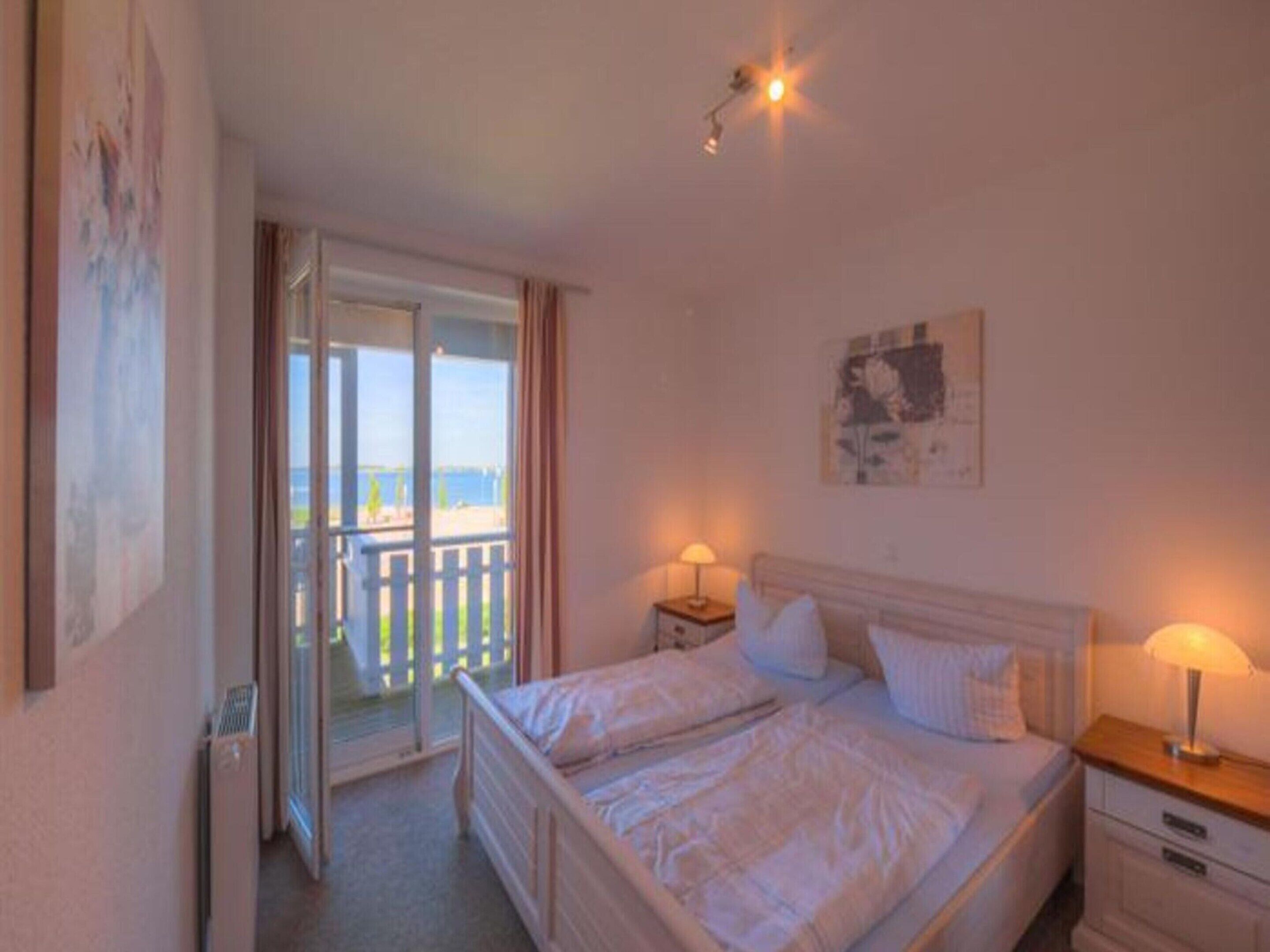 Une chambre à coucher comprenant un lit, deux tables de chevet avec des lampes, une fenêtre donnant sur un paysage agréable et une porte menant à un balcon.