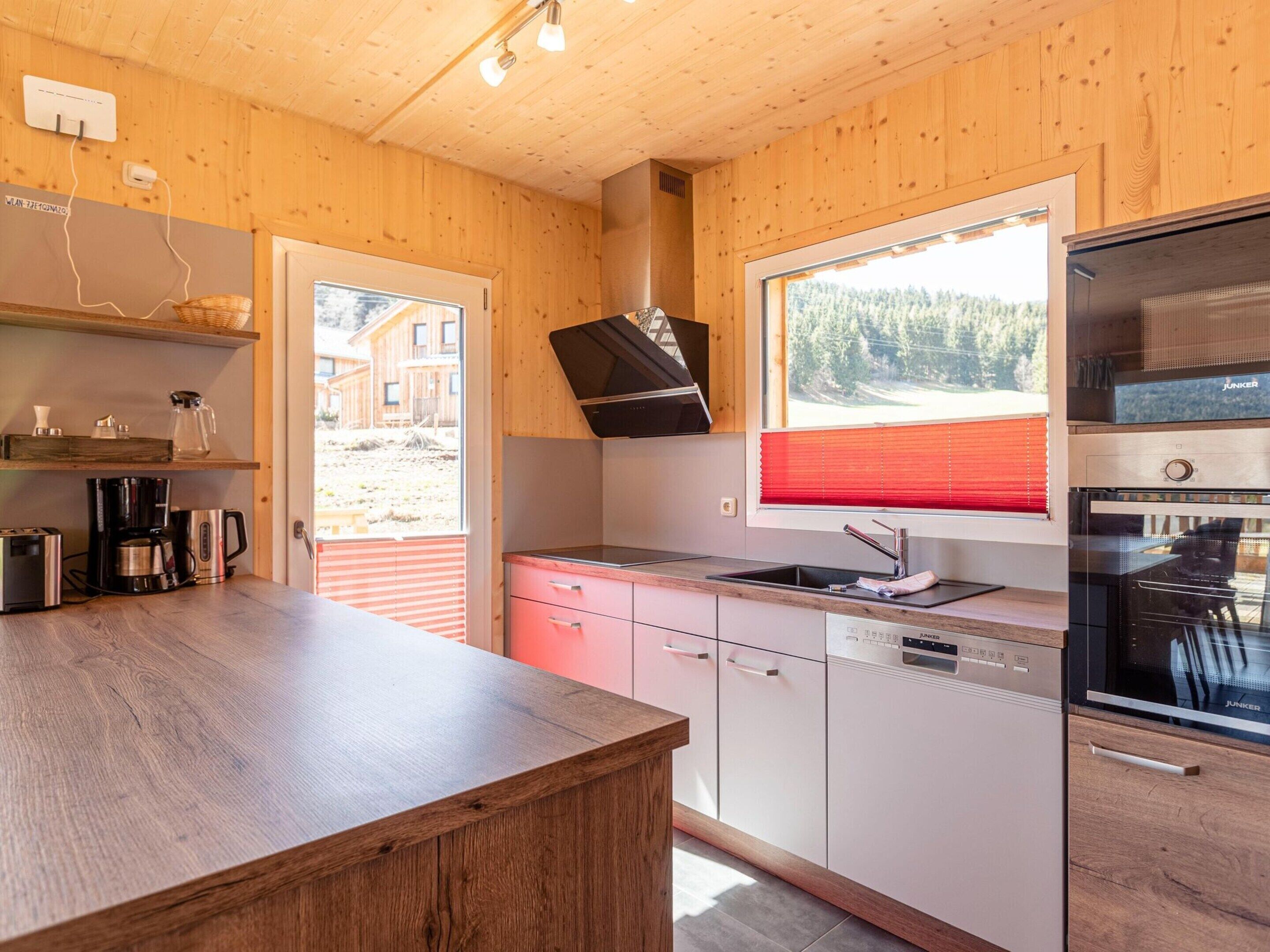 A modern kitchen with wooden walls, a built-in oven, and a window with a red blind.