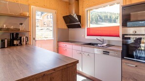 A modern kitchen with wooden walls, a built-in oven, and a window with a red blind. - Appealing Chalet With hot tub (Sankt Georgen am Kreischberg)