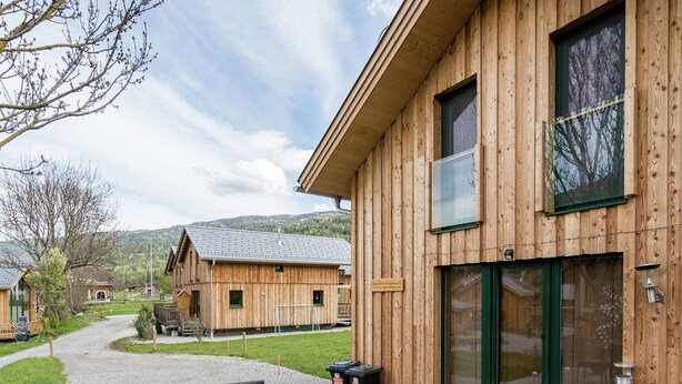 A wooden building with a patio area featuring a table and chairs, a large window, and a door. - Appealing Chalet With hot tub (Sankt Georgen am Kreischberg)