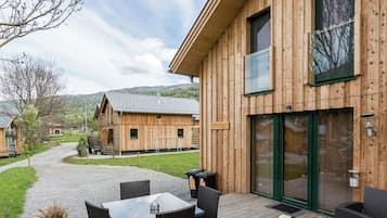 A wooden building with a patio area featuring a table and chairs, a large window, and a door.