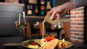 Een bord eten met een glas witte wijn, een hand giet saus, en een bakstenen muur op de achtergrond.