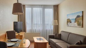 Una camera d'albergo con un tavolo da pranzo, un divano, una TV e un quadro raffigurante una spiaggia.