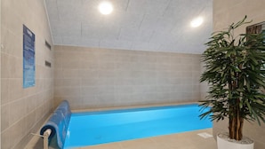 Una piscina con rivestimento interno blu, pareti piastrellate color beige e una pianta in vaso sulla destra.