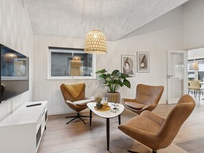 Ein modernes Wohnzimmer mit einem Flachbildfernseher, zwei Ledersesseln, einem Couchtisch mit Pflanze und einer Hängelampe.