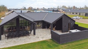 Un bâtiment moderne doté d’un toit en pente, de grandes fenêtres et d’un espace extérieur aménagé pour s’asseoir.