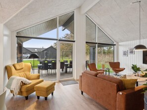 A modern living room with large windows, a sofa, a chair, and a dining area with a table and chairs. - 5 Star Holiday Home in Otterup (Otterup)