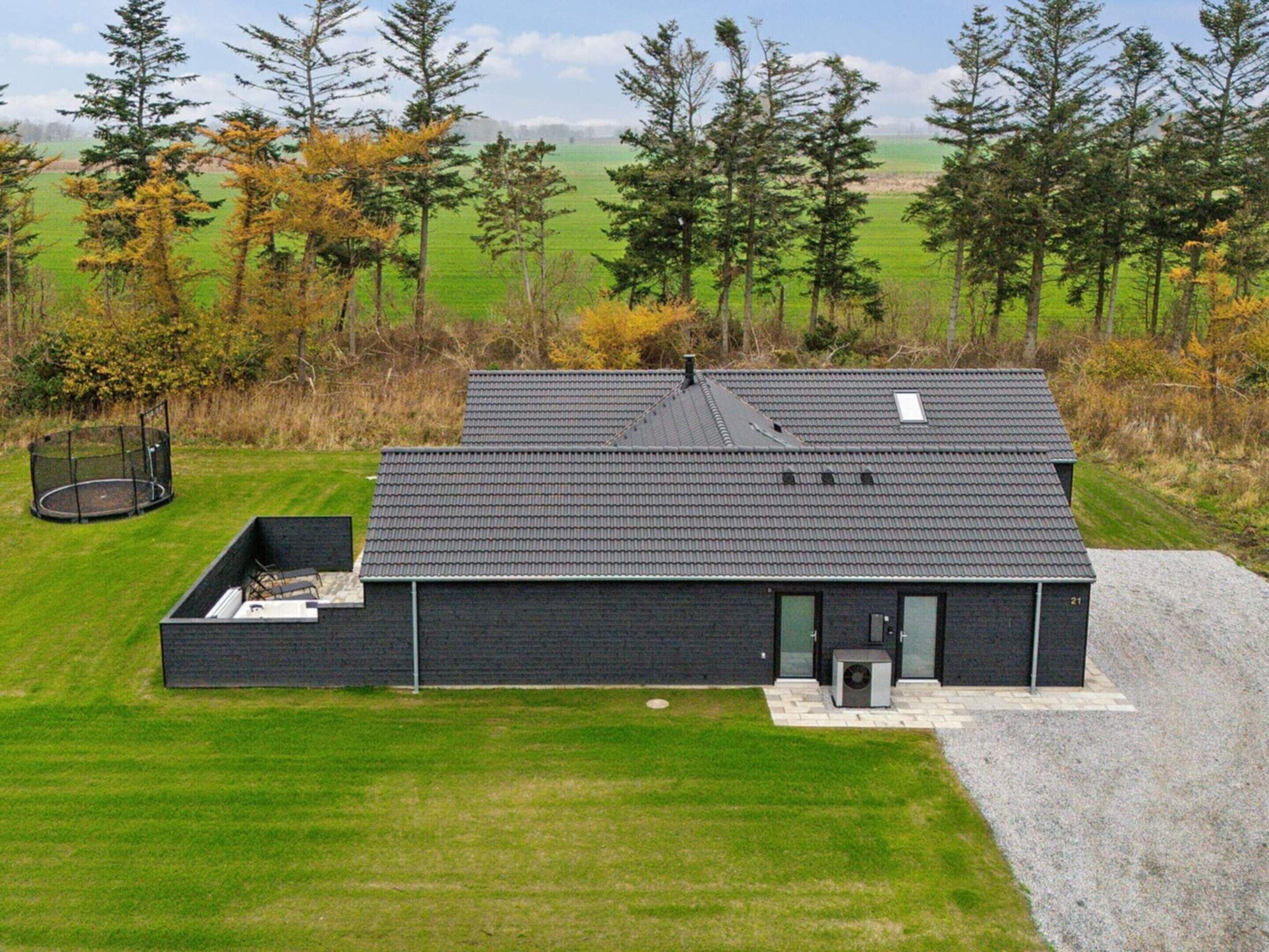 A modern two-story house with a dark roof and brick exterior, surrounded by a well-maintained lawn and a forested area.