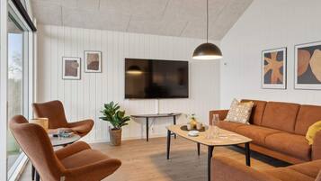 Ein modernes Wohnzimmer mit einer Couch, Sesseln, einem Couchtisch und einem an der Wand befestigten Fernseher.