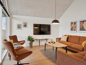 A modern living room with a sofa, armchairs, a coffee table, and a TV mounted on the wall. - 5 Star Holiday Home in Otterup (Otterup)
