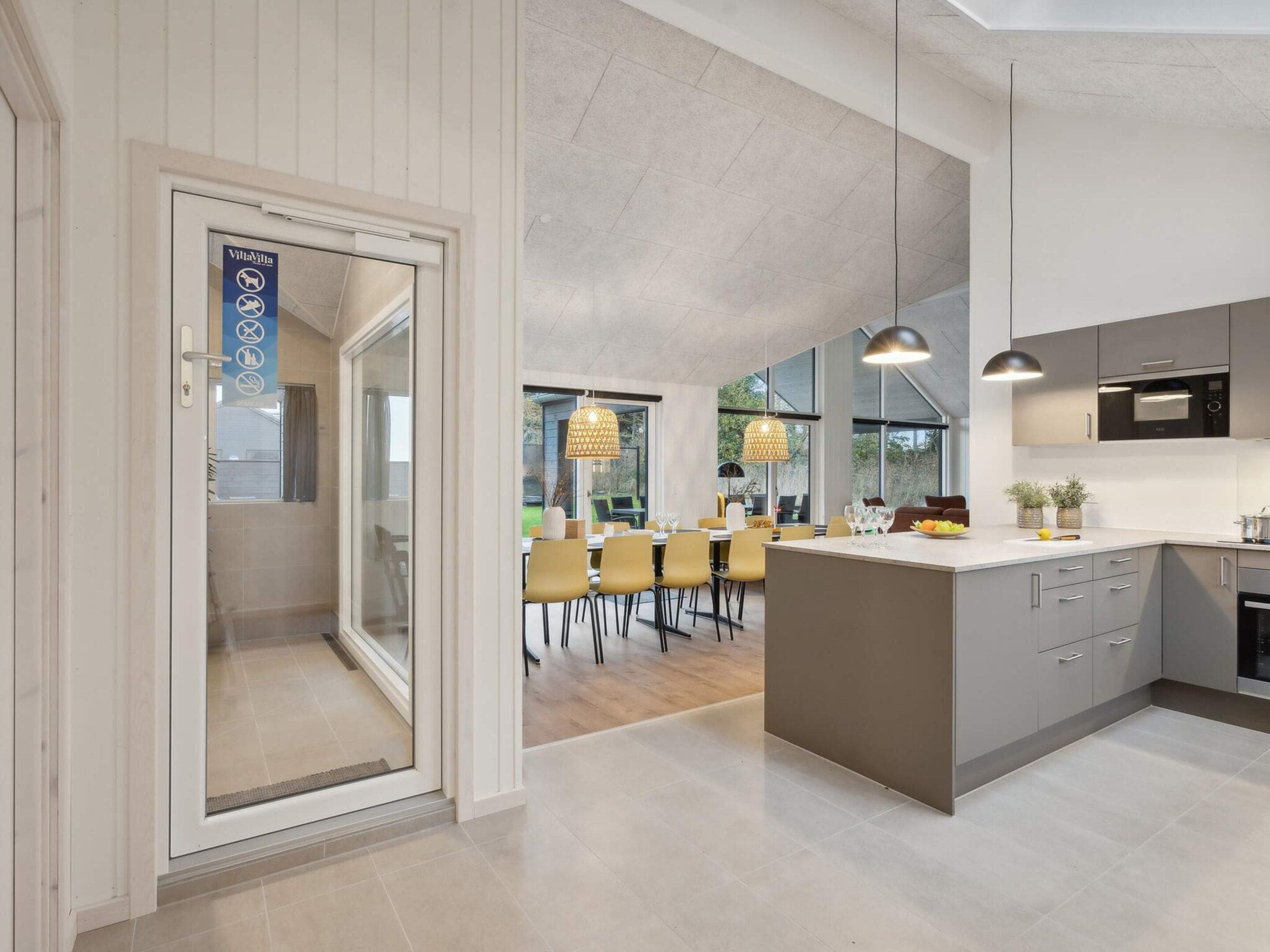 A modern kitchen with a central island, a dining area with yellow chairs, and a large window providing natural light.