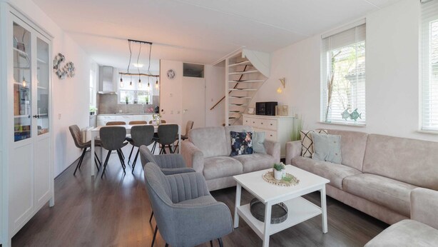 A modern living room with a sofa, armchairs, and a coffee table. There is a staircase leading to an upper level. - Holiday Home in Zeeland With Garden Terrace (Wemeldinge)