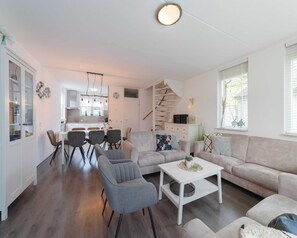 Uma sala de estar moderna com sofá, poltronas e mesa de centro. Escada leva a um andar superior.