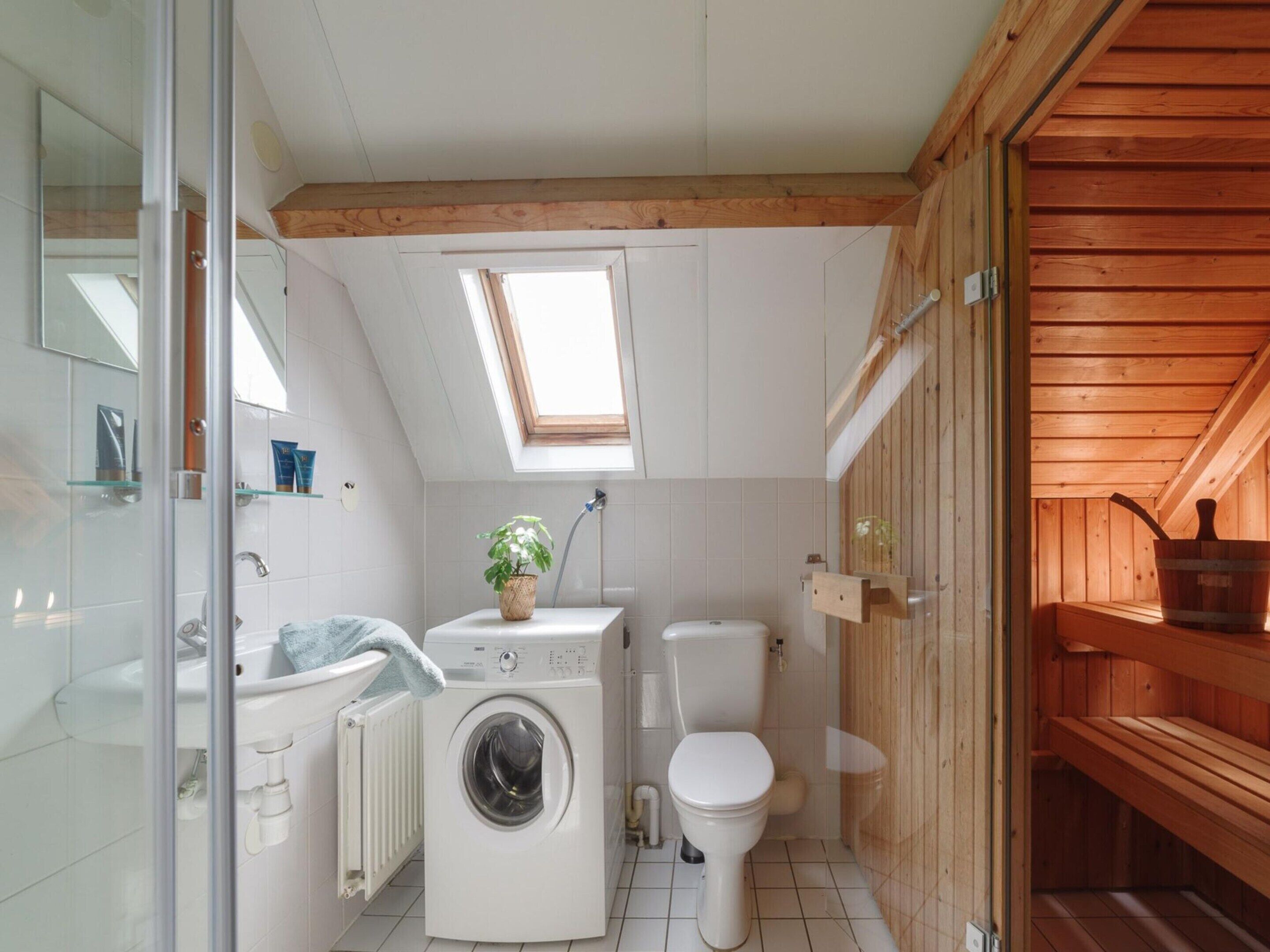 Une salle de bain moderne et compacte, dotée d’un puits de lumière, d’un lave-linge, de toilettes et d’un espace sauna en bois.
