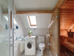 A compact, modern bathroom with a skylight, a washing machine, a toilet, and a wooden sauna area.