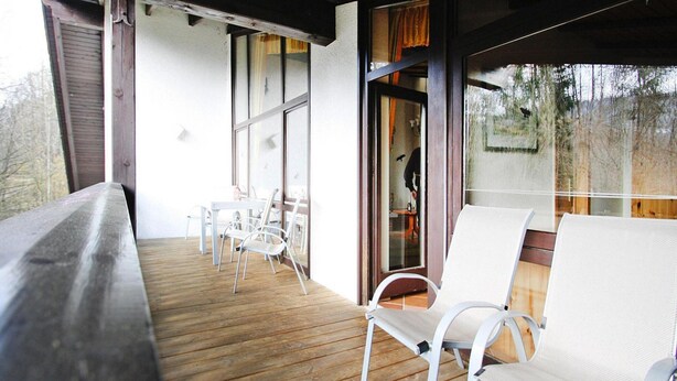 A covered outdoor area with a wooden deck, white metal chairs, and a table.