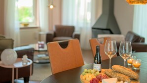 A dining table with a bottle of wine, glasses, cheese, grapes, and bread in a modern, well-lit room with a fireplace and comfortable seating. - Bungalow in Sondel Near Slotermeer Lake (Sondel)