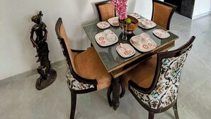 A dining area with a table set for four, surrounded by chairs with patterned upholstery. A Buddha head sculpture is mounted on the wall above the table. - Fun O Peace (Noida)