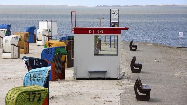 A beachside kiosk with a sign reading "DLRG" and a clock above it. - Ferienhaus Albatros in Nessmersiel (Dornum)