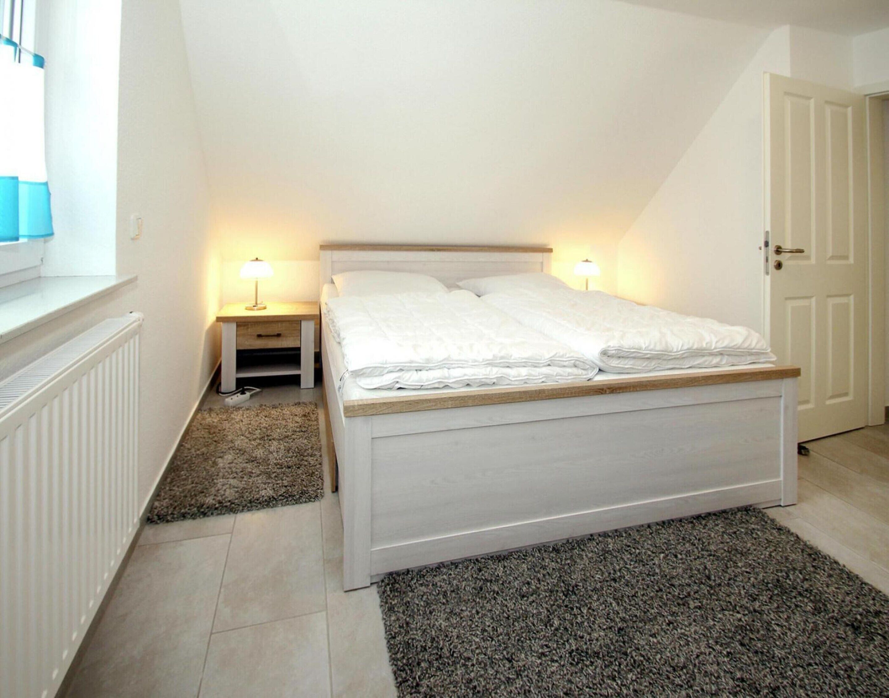 A bedroom with a bed, two bedside tables with lamps, a radiator, a carpet, and a door.