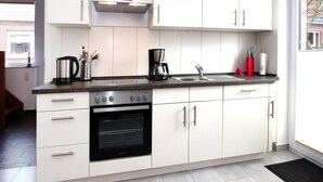 A modern kitchen with white cabinets, a black oven, a stainless steel range hood, and a double sink. - Ferienhaus Albatros in Nessmersiel (Dornum)