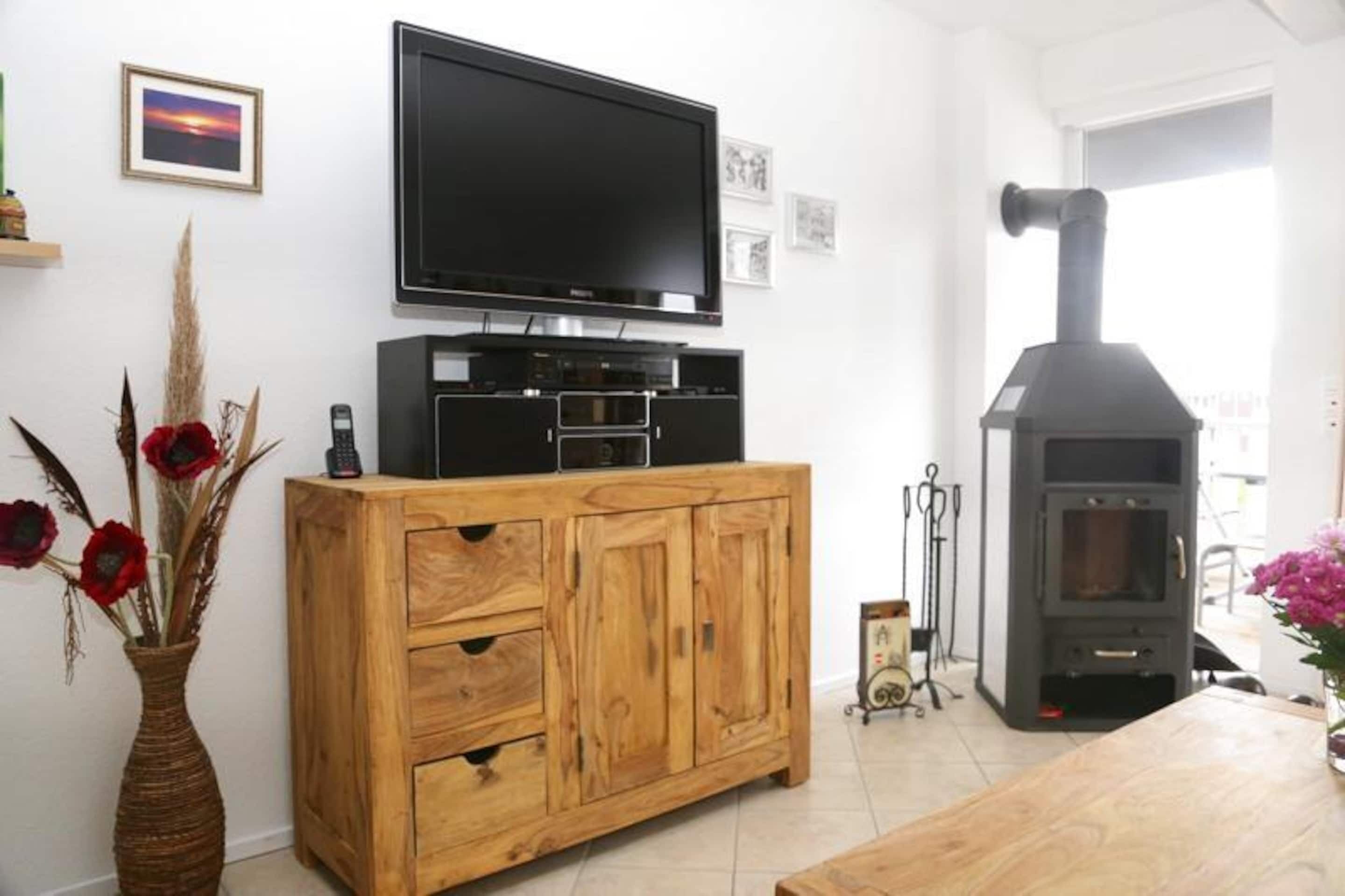 Una sala de estar con un aparador de madera, un televisor de pantalla plana, una chimenea y un florero con flores rojas.