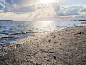 Ein Strand mit Sand, Wasser und einer fernen Küste.