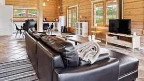A modern log cabin interior with a leather sofa, dining area, kitchen, and a television.