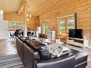 A modern log cabin interior with a leather sofa, dining area, kitchen, and a television.