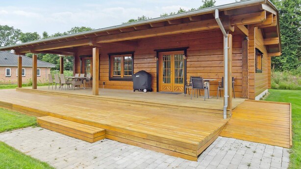 A wooden cabin with a covered porch, outdoor seating, and a barbecue grill.